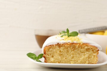 Tasty lemon cake decorated with icing, zest and mint served on white table, closeup. Space for text
