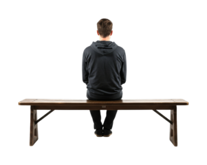 Young man wearing a dark hoodie sits on a rustic wooden bench, seen from behind, appearing contemplative and solitary in a studio setting