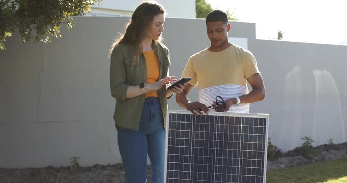 Diverse coworkers connecting MC4 cables to solar panel following tablet prompts in backyard