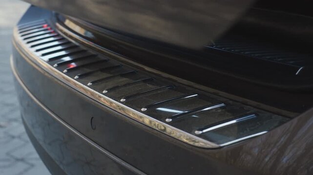 Car trunk automatic closing with chrome bumper sill detail and clean lock sound, close up rear view outdoors