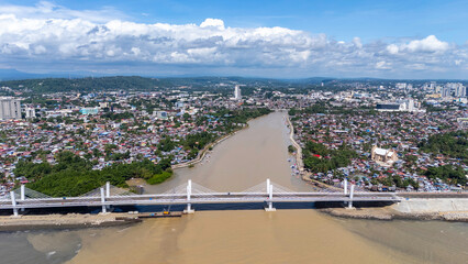 defaultWide aerial view showing Bancasa Bridge crossing the Davao River with dense downtown cityscape, urban shoreline, and surrounding coastal environment visible under clear daytime skies.