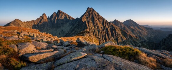 Majestic mountain range under a clear blue sky, with foreground rocks & golden-hued vegetation