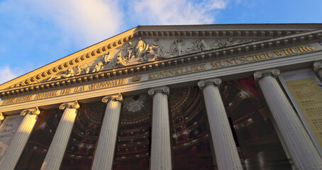 Naklejka premium BRUSSELS, BELGIUM - NOVEMBER 26, 2025 - Iconic neoclassical La Monnaie opera building facade at golden hour under a blue sky