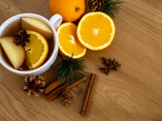 Warm winter drink with apple and orange slices, star anise and spices surrounded by pine branches, cinnamon and festive decorations — cozy homemade seasonal beverage still life