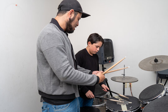 Teacher demonstrating proper drumstick grip while the student plays the drums. Drum technique instruction, rhythm learning, music education, private percussion training