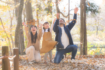 逆光の美しい秋の公園で落ち葉遊びを楽しむ家族の笑顔・親子の幸せな秋の思い出ポートレート　お出かけやレジャーのイメージ