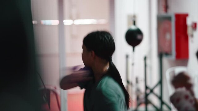 Young female boxer training punching bag at gym