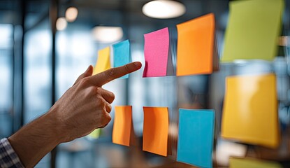 Hand pointing at colorful sticky notes arranged on glass surface in office