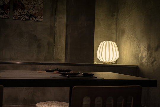 A dimly lit modern dining area with black dishes, floral wall art, and a glowing lamp, creating a cozy ambiance.