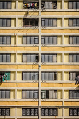 A multi-story residential building with metal grilles, laundry, and yellow-beige facade, showing symmetrical urban living.