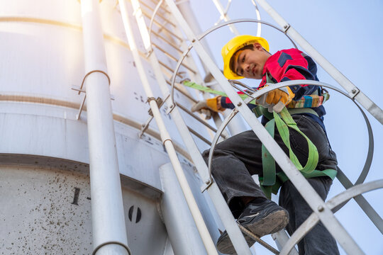 Close-up, low-angle shot of a construction worker in a safety harness climbing a cement silo ladder, showing compliance with safety regulations.