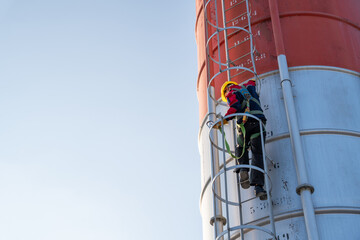 a worker climbing the fixed ladder of a tall cement silo, emphasizing industrial height and safety.