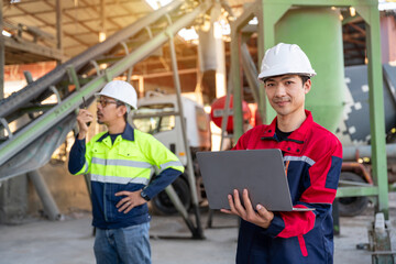 Two construction managers using a laptop and walkie-talkie for coordination and digital planning at a small ready-mix concrete plant.