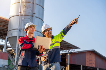 Front view of two construction managers using a laptop and radio to communicate and manage operations at a small ready-mix concrete plant.