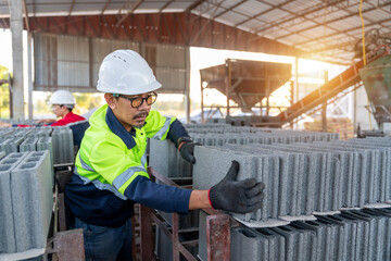 A construction manager wearing a safety vest inspects the quality of fresh concrete cinder blocks at a small building material manufacturing plant.