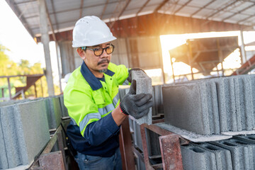 A construction manager carefully lifts and inspects the quality of a fresh concrete cinder block at...
