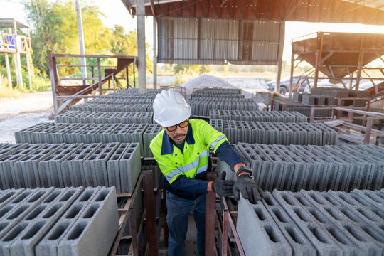 A construction manager inspects rows of fresh concrete cinder blocks at a small building material manufacturing plant, focusing on stock and quality.