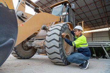 A construction manager carefully inspects the large tire of a wheel loader, focusing on maintenance and heavy equipment operations at the job site.