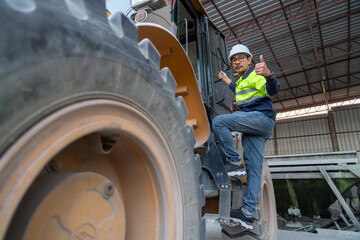 A confident construction manager gives a thumbs-up while climbing into a wheel loader, signifying successful operation and management.
