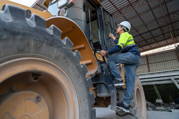A construction manager in a safety vest climbs into the cab of a wheel loader, preparing to oversee heavy equipment operation at the job site.