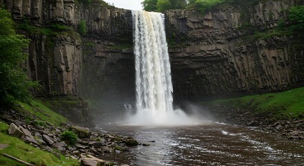 Large waterfall cascades down columnar basalt cliffs, creating mist over a brown pool