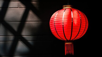 Obraz premium A vibrant red lantern with black detailing and decorative fringe casts soft shadows against a dark wall.