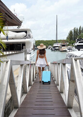 Young woman with small blue luggage walks near the boat marina