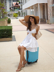 A woman is comfortably sitting on a blue suitcase at the boat marina