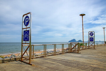 A beach with a parking sign and a bicycle parking sign, with an island in the middle of the sea in the background.