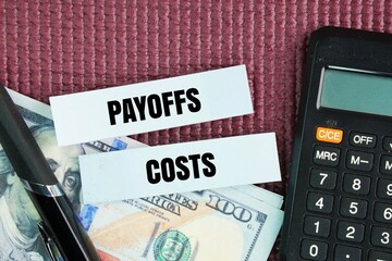 Pen, paper money and calculator with the words Payoffs and Costs. payoffs and costs are learned through reward prediction errors