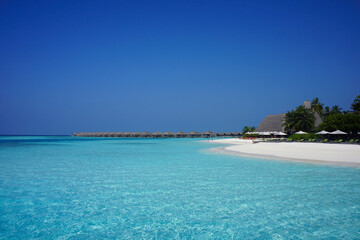 Fototapeta premium Overwater Bungalows and White Sand Beach in the Shallow Turquoise Sea of Maldives