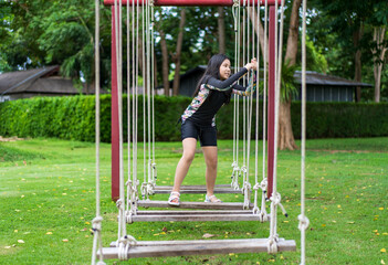 asian child fun swing on ropes and walking on swings or young kid girl person enjoy playing jumanji activity to adventure on playground lawn garden at school or holiday in resort by outdoor theme park