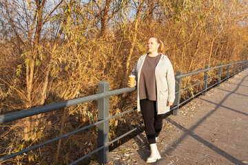 Casual middle-aged woman enjoys a coffee break while walking in park.