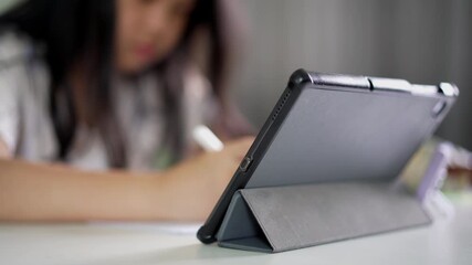 closeup tablet with blur asian child student study online or young kid girl writing or notes on paper with computer and doing homework or people learn from homeschool and back to school by smartphone - Powered by Adobe