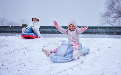 Joyful Children Sledding Down a Snowy Hill &ndash; Winter Fun and Laughter on Inflatable Sleds. Winter Thrill Ride