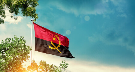 Angola national flag waving in the sky behind the tree. The flag blowing with beautiful sunlight. Angola national flag for independence day.