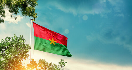 Burkina Faso national flag waving in the sky behind the tree. The flag blowing with beautiful sunlight. Burkina Faso national flag for independence day.