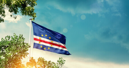 Cabo Verde national flag waving in the sky behind the tree. The flag blowing with beautiful sunlight. Cabo Verde national flag for independence day.