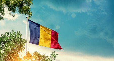 Chad national flag waving in the sky behind the tree. The flag blowing with beautiful sunlight. Chad national flag for independence day.