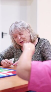 Senior woman playing a parcheesi board game with her caregiver