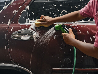Photo of a man wearing a t-shirt washing or cleaning his car alone. Washing the car with soap and water during the day.