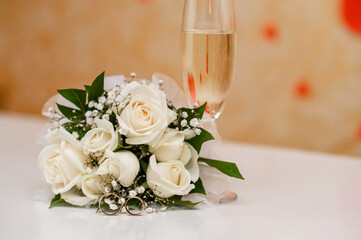 white rose bouquet on wedding table, accompanied by a glass of champagne. peaceful and elegant mood for a wedding. white rose flowers perfect scene of wedding anticipation and joy. festive background.