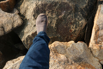 Person walks carefully on large coastal boulders of the Shangumugham Beach sea wall, wearing casual shoes and jeans in warm evening light.