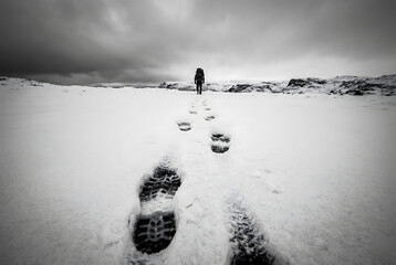 Lone hiker walks through a vast snowy landscape leaving footprints winter backpack