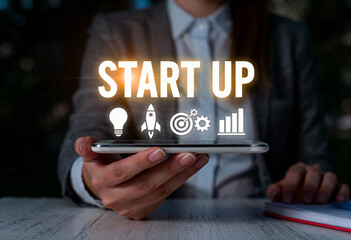 Woman showing start up text with light bulb rocket target gear and growth graph icons hovering over a smartphone