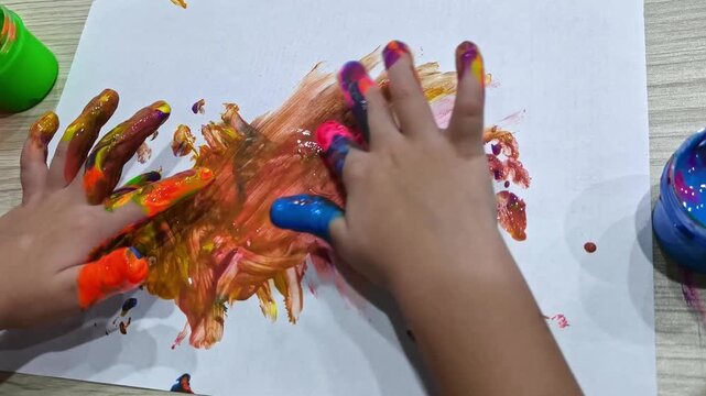 Children's hands smear bright finger paints on a piece of paper, creating an abstract drawing and developing creativity.