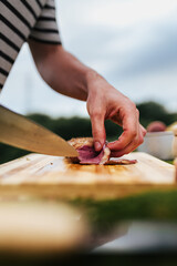 Hand slicing raw meat on a wooden cutting board outdoors