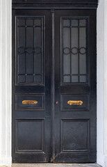 Classic wooden double door with decorative panels and vintage handles, framed by marble walls, showcasing traditional architecture and elegant historic craftsmanship.