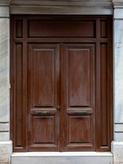 Classic wooden double door with decorative panels and vintage handles, framed by marble walls, showcasing traditional architecture and elegant historic craftsmanship.