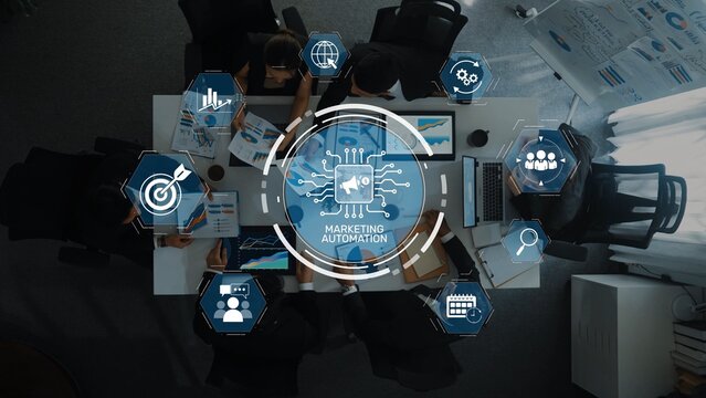 A top-down view of a business meeting focusing on marketing automation, featuring professionals engaged in discussions and interactive digital visuals showcasing key strategies. Raster